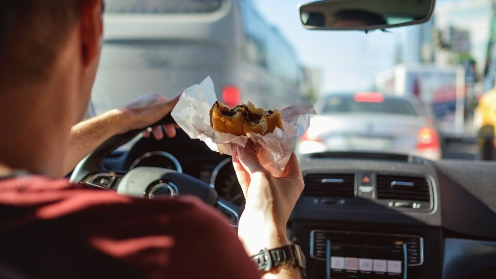 Man driving car while eating hamburger