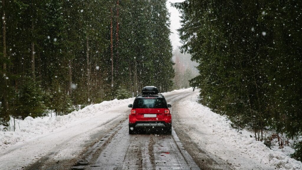 Red car with roof rack driving on a forest road in winter