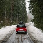 Red car with roof rack driving on a forest road in winter