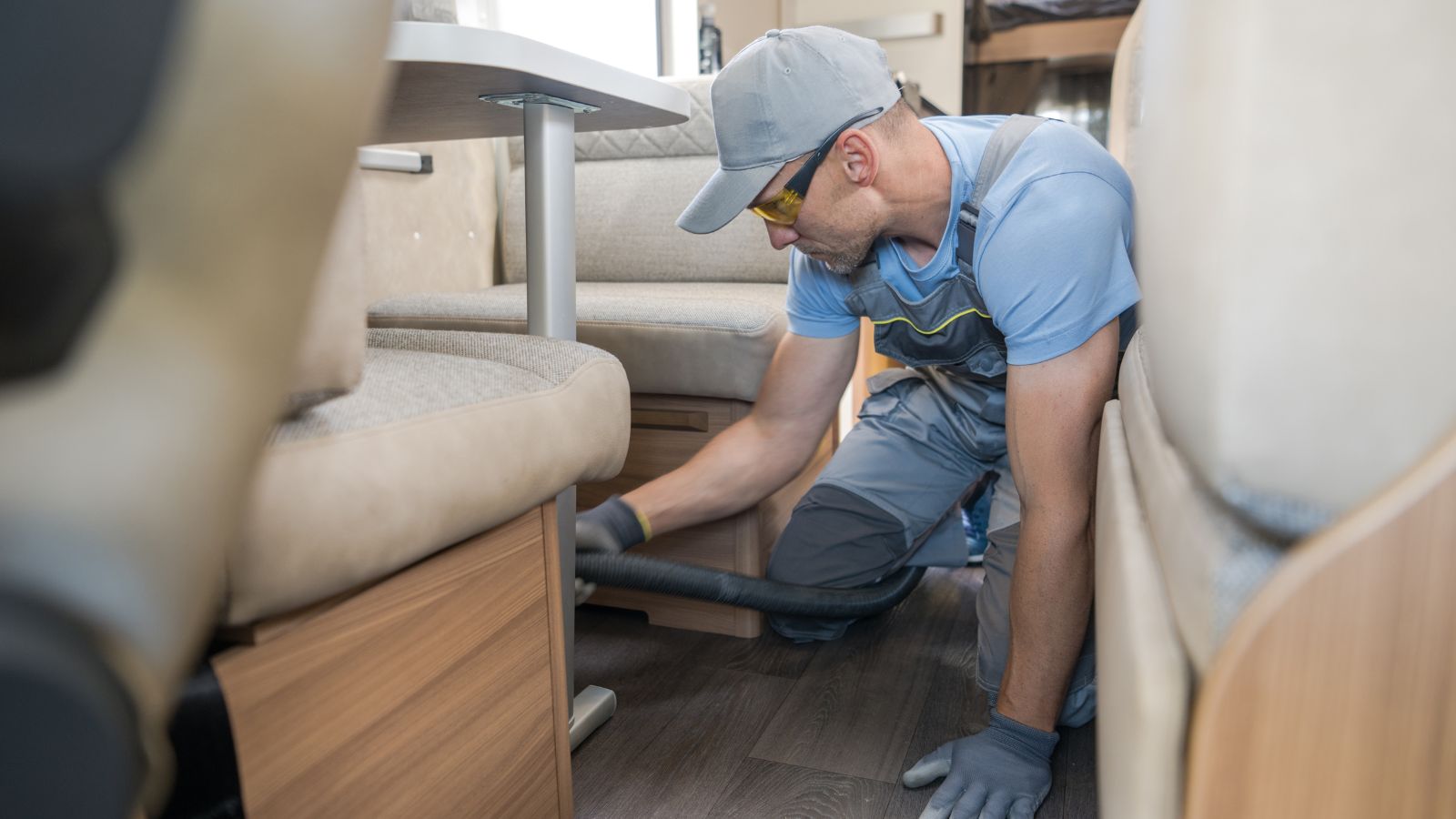 Vacuuming Floor Under the Beige Sofa in Modern RV. Interior Cleaning
