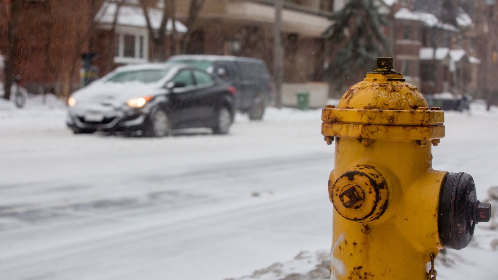 TORONTO, CANADA - FEBRUARY 12, 2019: CLOSE UP OF YELLOW FIRE HYDRANT WITH OUT OF FOCUS CAR IN SNOWY