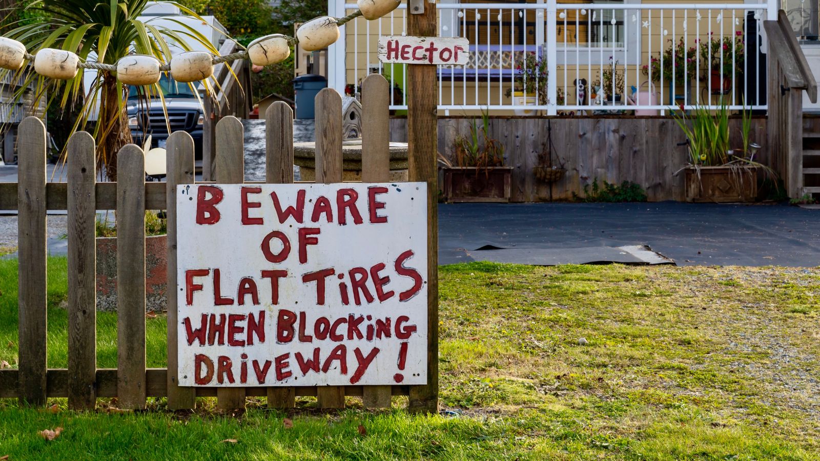 Funny warning sign on a fence along public road tells people not to block a private driveway - Beware of flat tires when blocking driveway