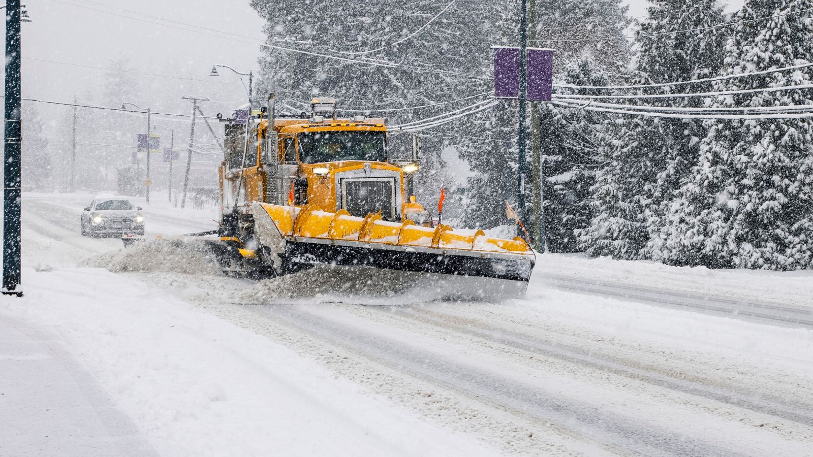 Modern yellow snowplow driving along road in winter removing snow
