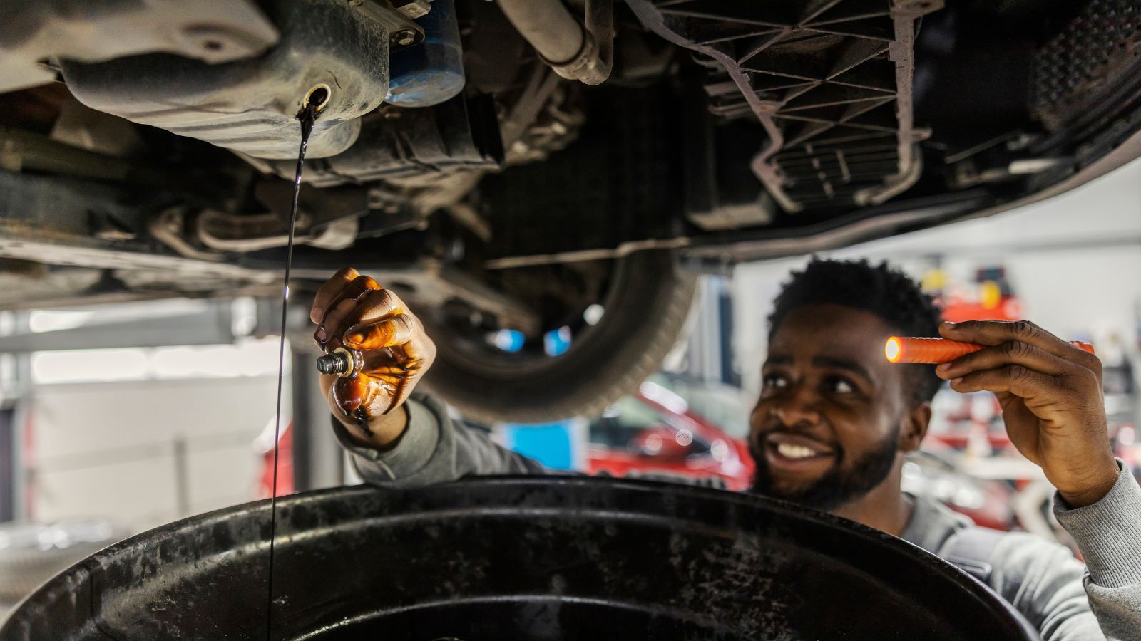 technician changing oil on car under chassis