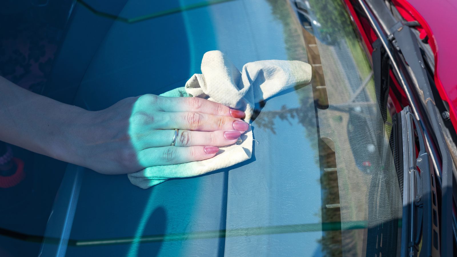 Woman's hand wiping car front panel with a microfiber at home. Car wash