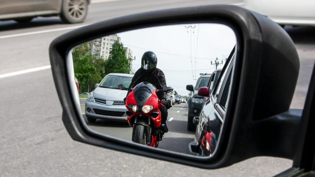 side mirror of the car reflects a motorcyclist