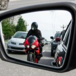 side mirror of the car reflects a motorcyclist